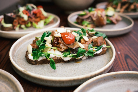 Een bord met een belegde boterham met ricotta, waterkers en tomaat