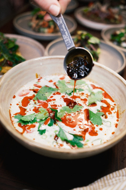 Een bowl met kokossoep en iemand die er crispy chili olie in drapeert