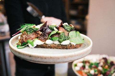 Een bord met een broodje met witte ricotta, groene pesto en paarse bietjes 