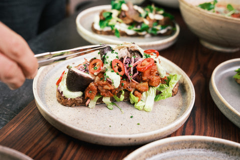 Een chef lefgt met een pincet een finishing touch aan een broodje met geroosterde aubergine 